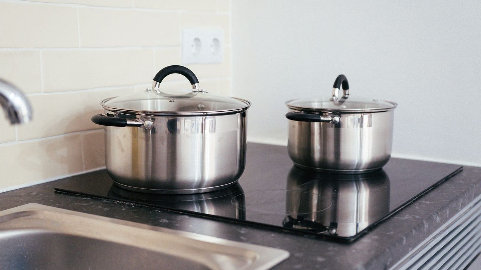 Two stainless steel pots with glass lids on an induction cooktop.