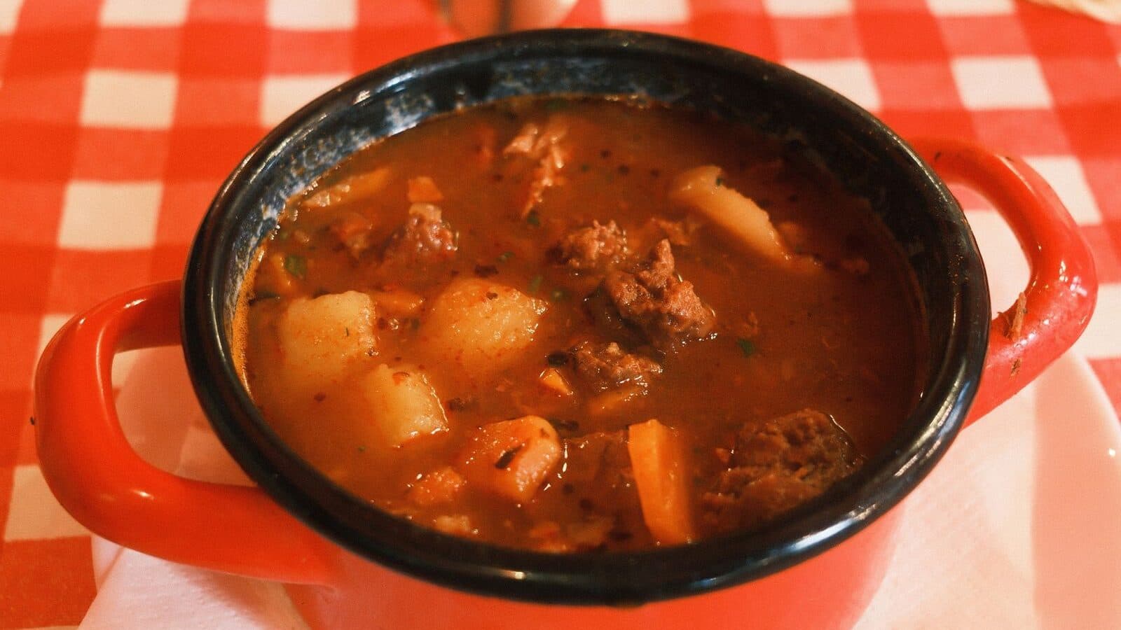 A pot of goulash stew on a red checkered tablecloth