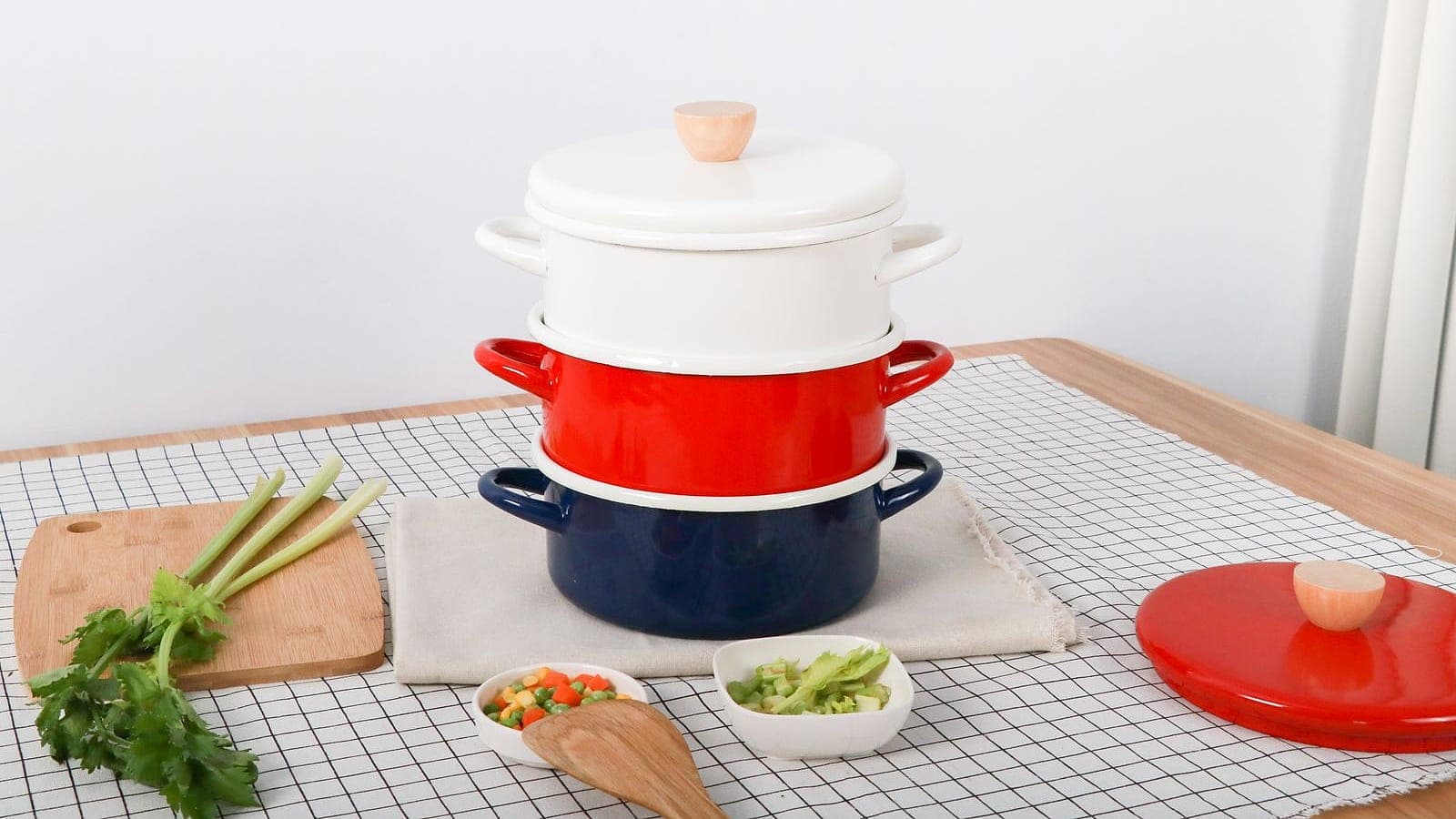A stack of colorful red, white, and navy enameled cookware pots on a kitchen table