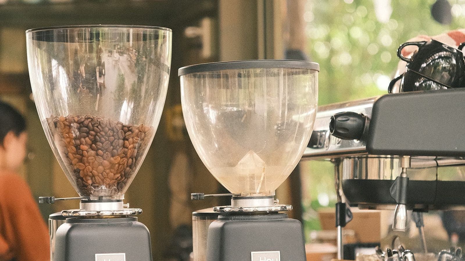 Two burr coffee grinders with bean-filled hoppers next to an espresso machine.