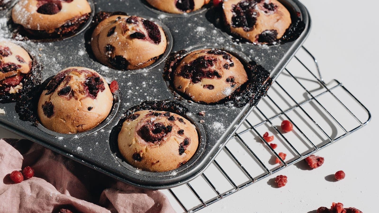 Blueberry muffins in a muffin pan beside a cooling rack.