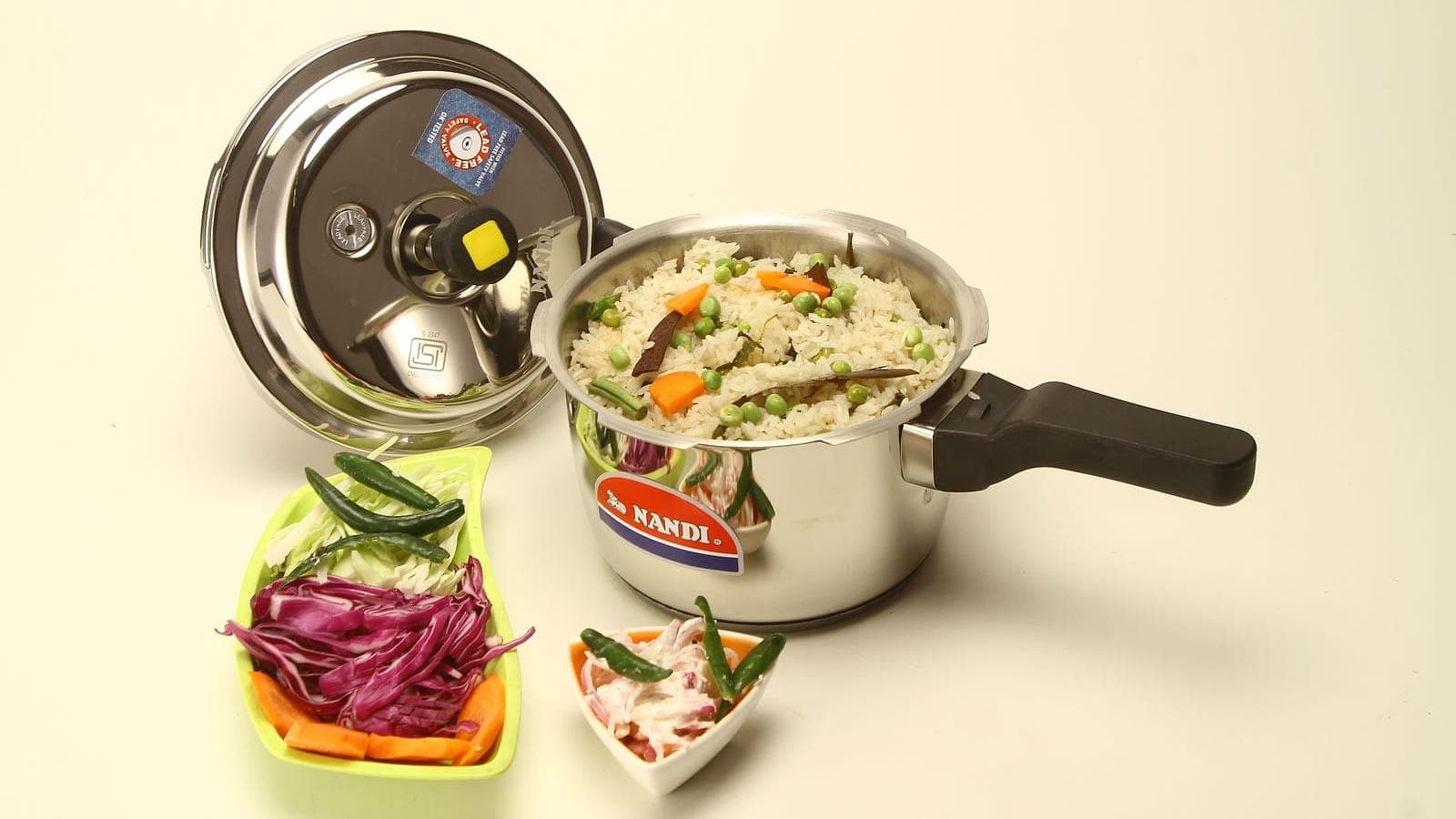 A stainless steel pressure cooker beside a bowl of vegetable rice.