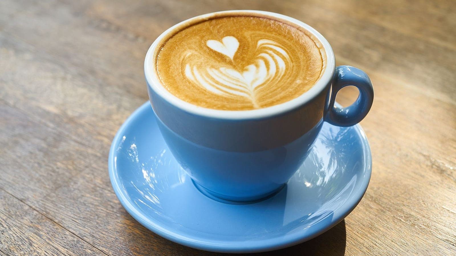 A latte with leaf latte art served in a blue cup on a wooden table.