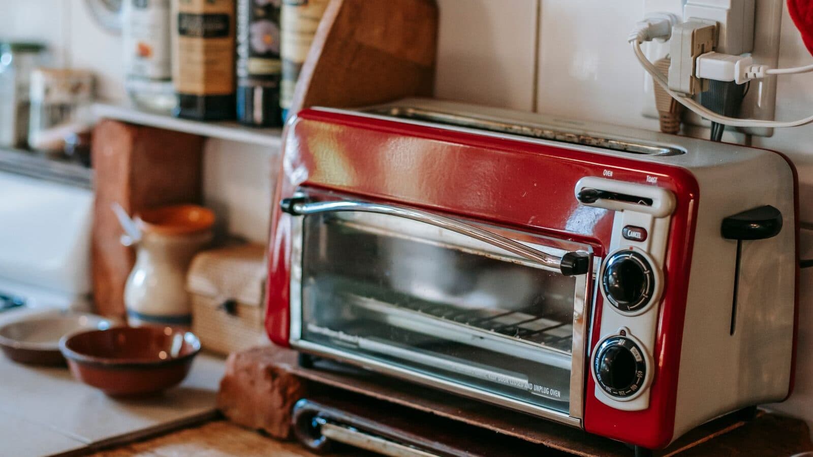 A stainless and red countertop toaster oven on a rustic wooden kitchen counter