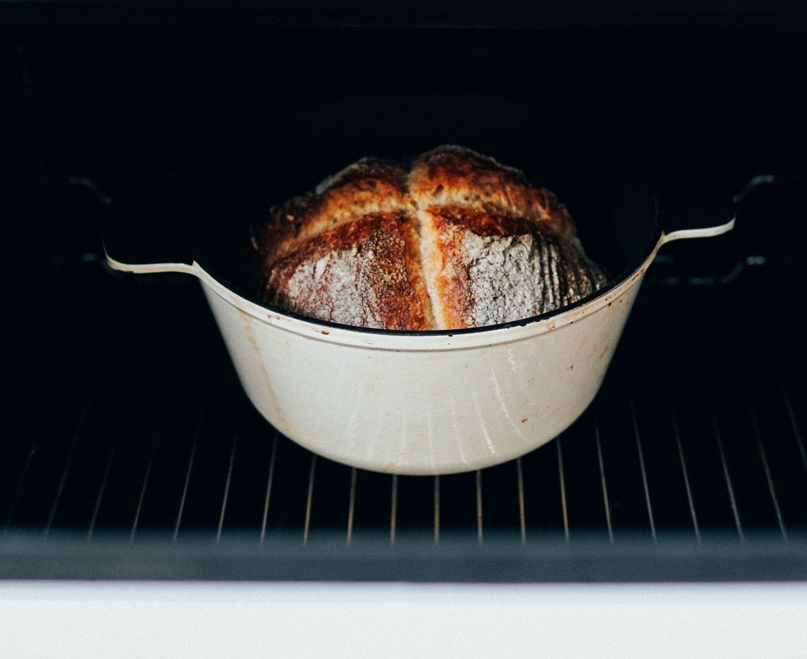 A crusty sourdough loaf baking inside a white enameled Dutch oven