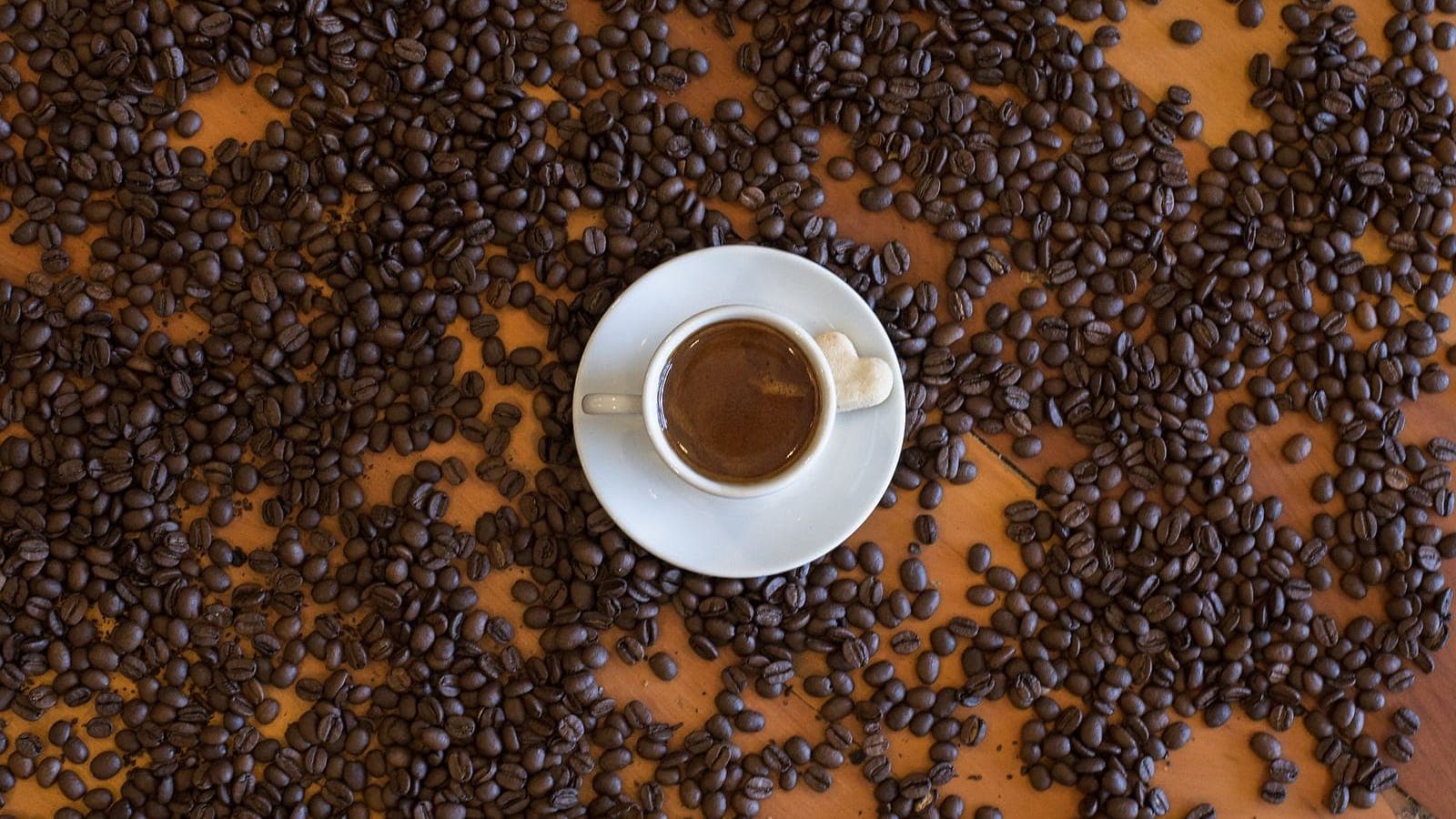 An overhead view of an espresso in a white cup surrounded by scattered roasted coffee beans.