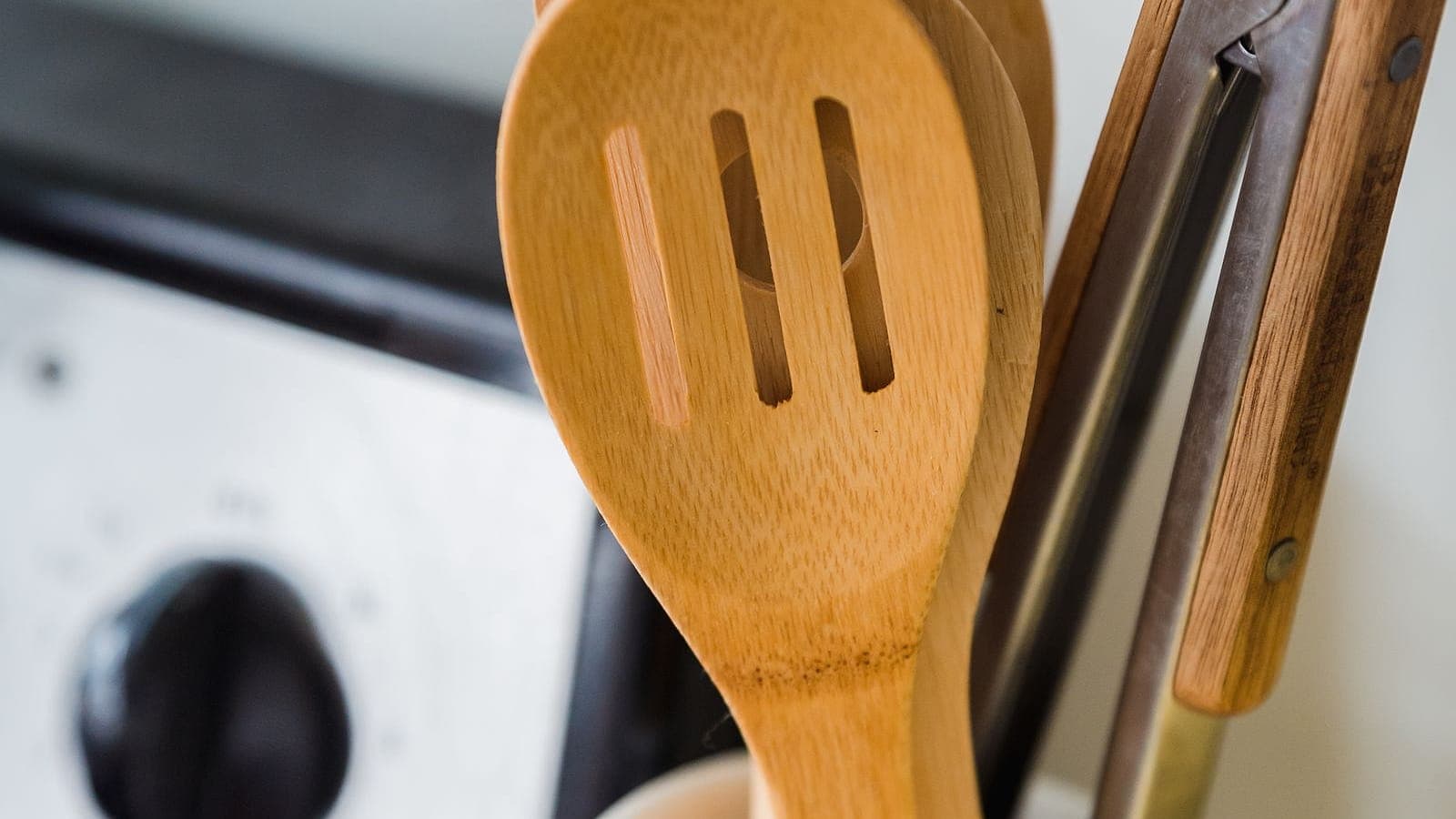 Wooden cooking utensils in a ceramic crock beside a stovetop in a small kitchen