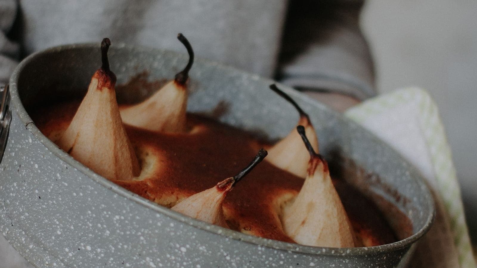 Poached pears in a round baking dish held with a towel.
