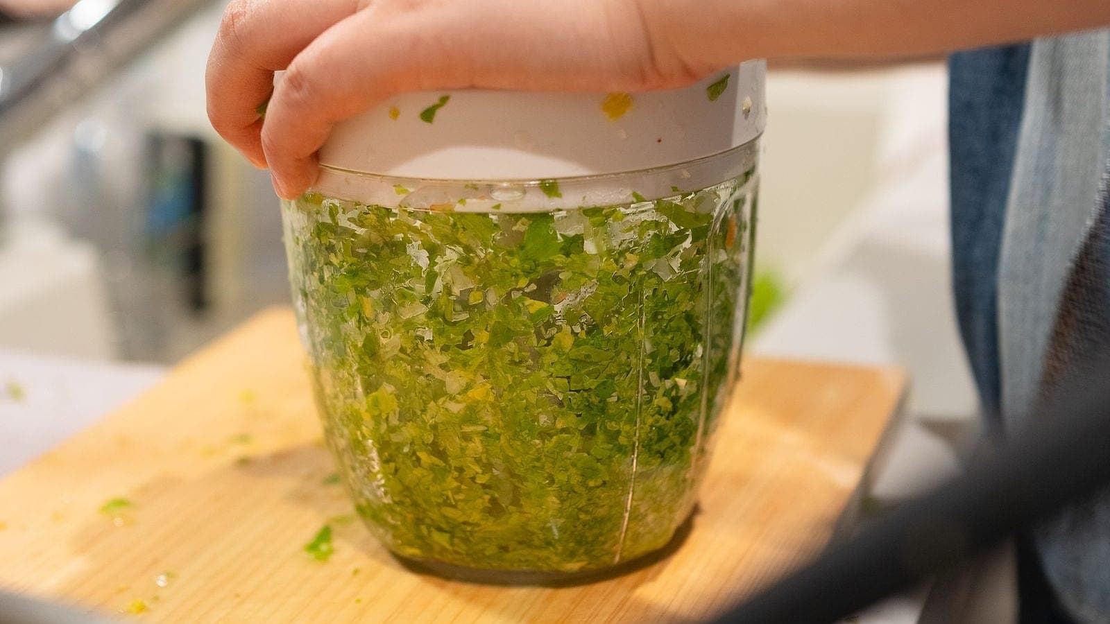 Hands pressing a food chopper filled with chopped herbs.