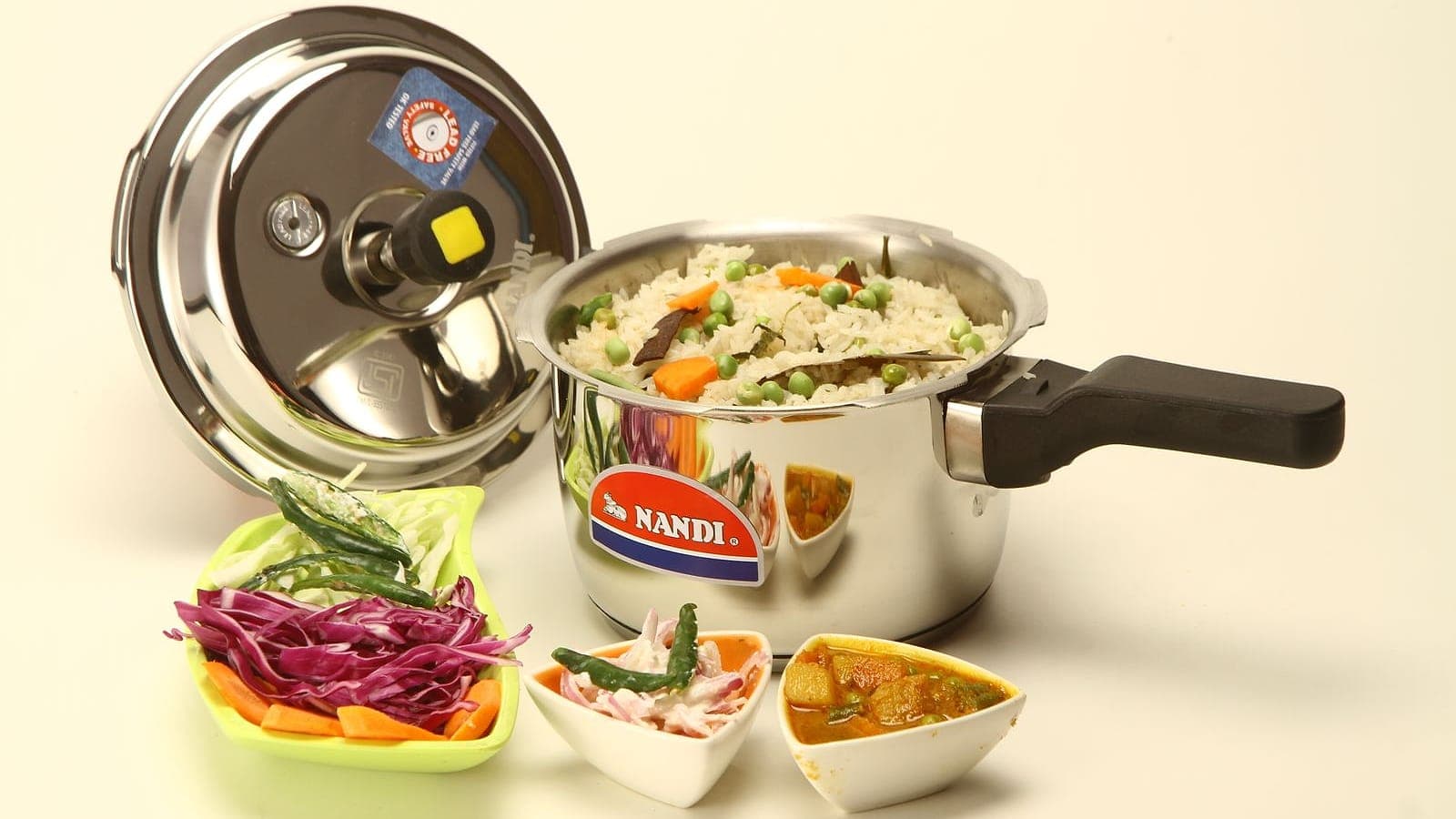 A stainless steel pressure cooker with its lid beside cooked rice.