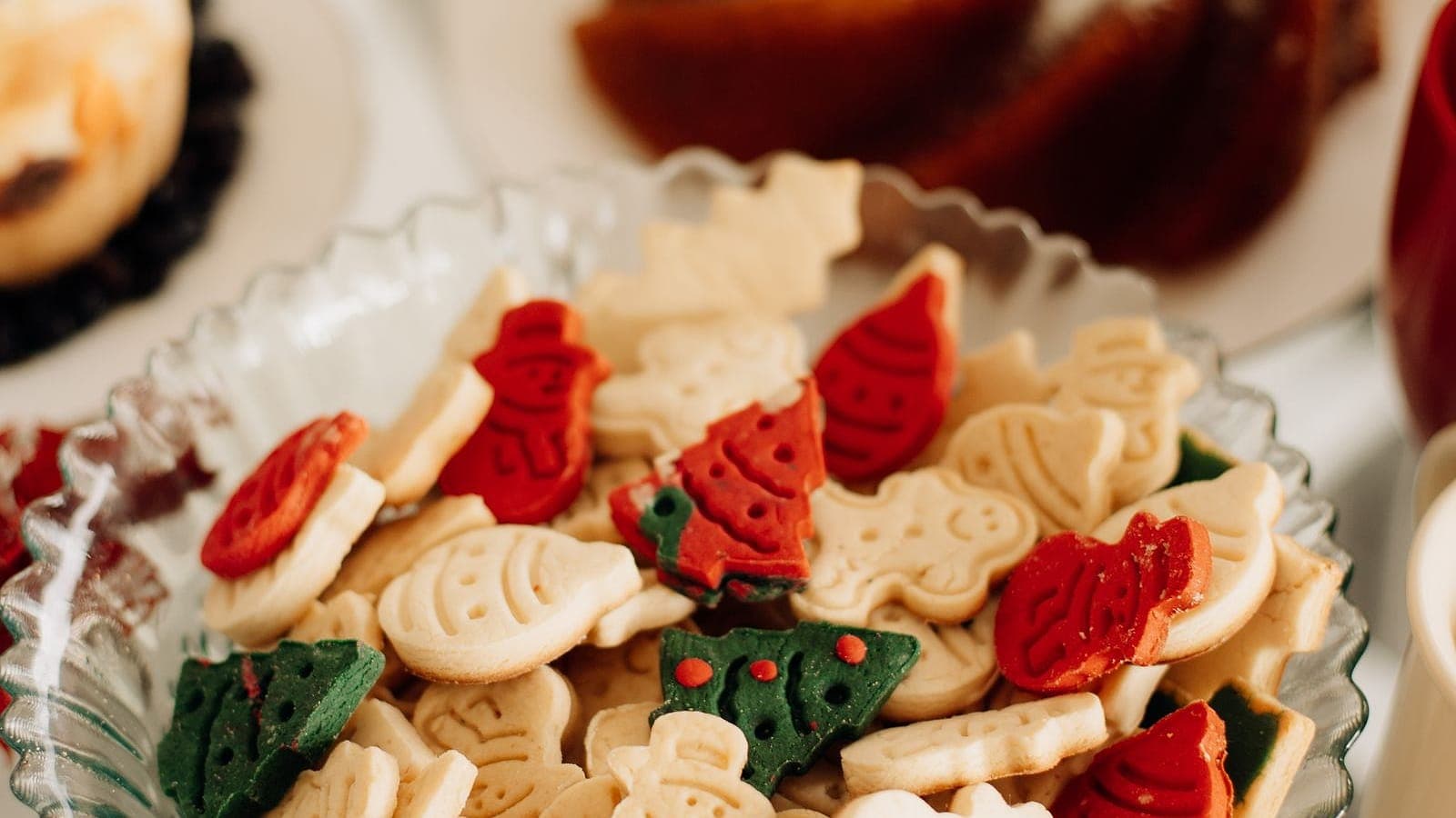 A dish of festive holiday cookies on a table with a bundt cake in the background