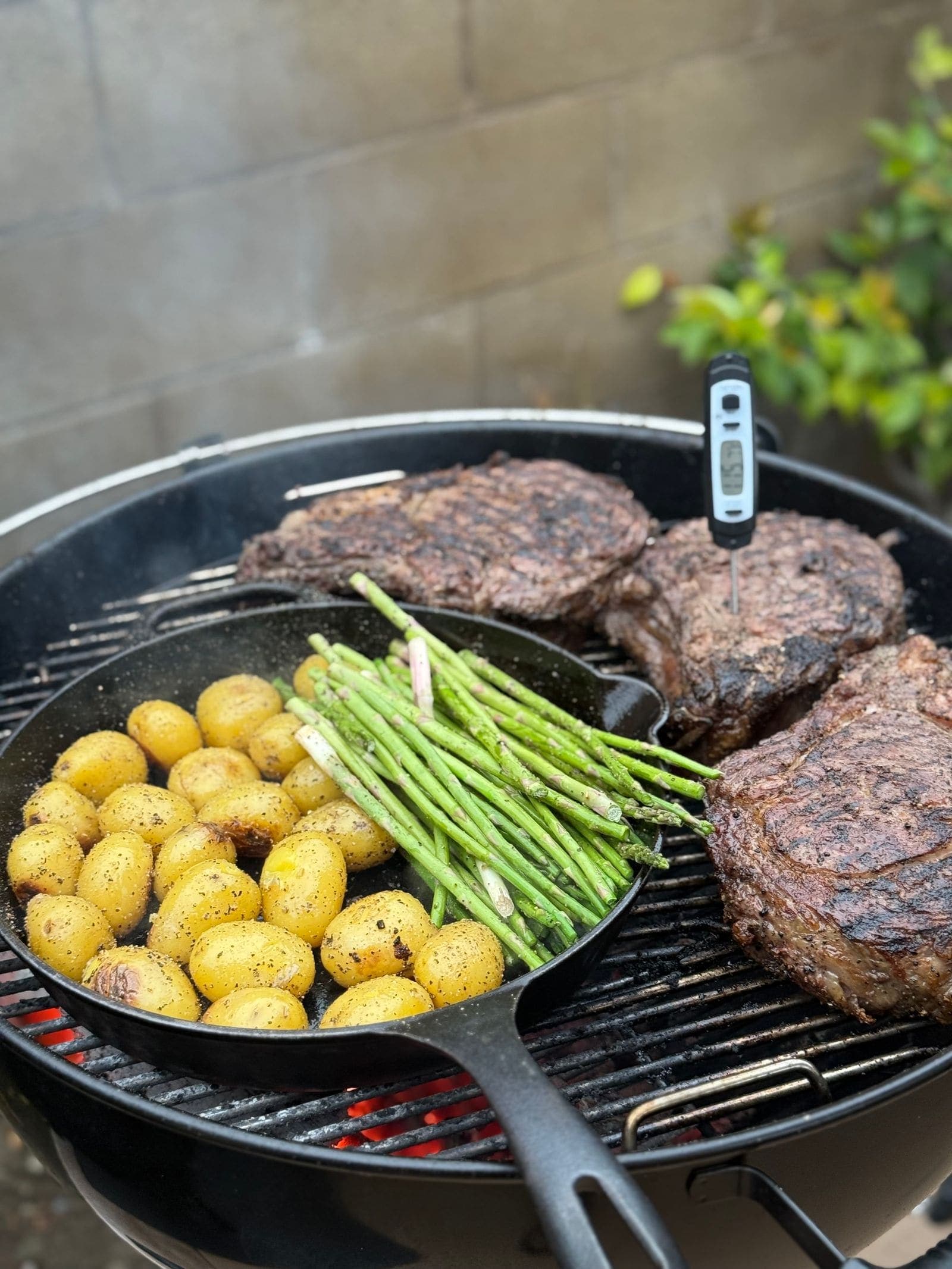An instant-read thermometer probing a thick steak on a charcoal grill