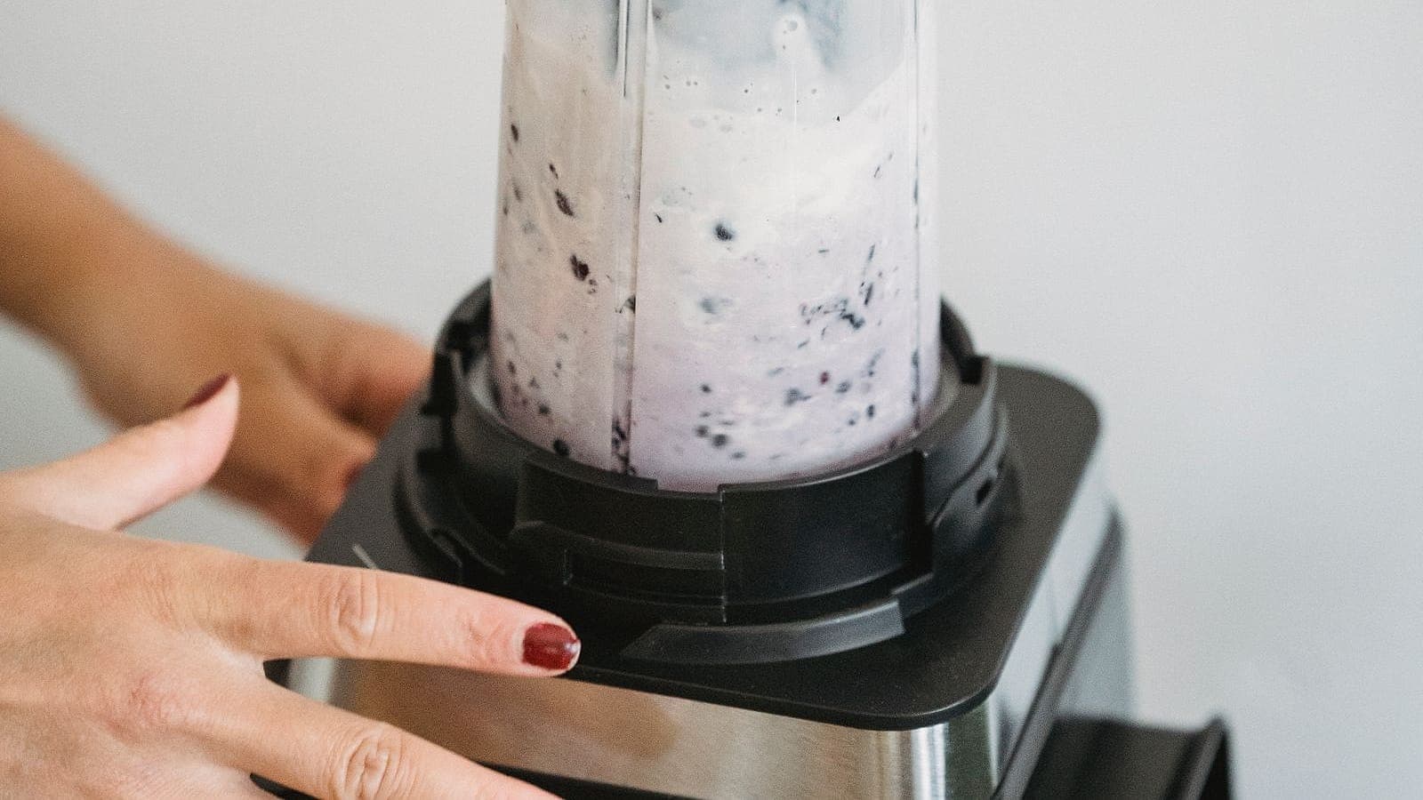 A hand operating a high-performance countertop blender full of berry smoothie