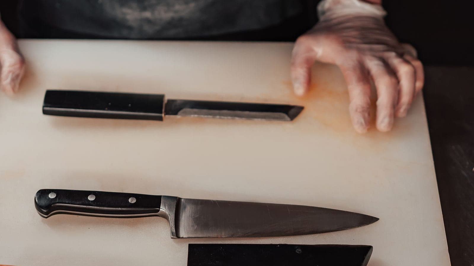 Three kitchen knives — a Western chef's knife and two Japanese-style knives — laid out on a white cutting board