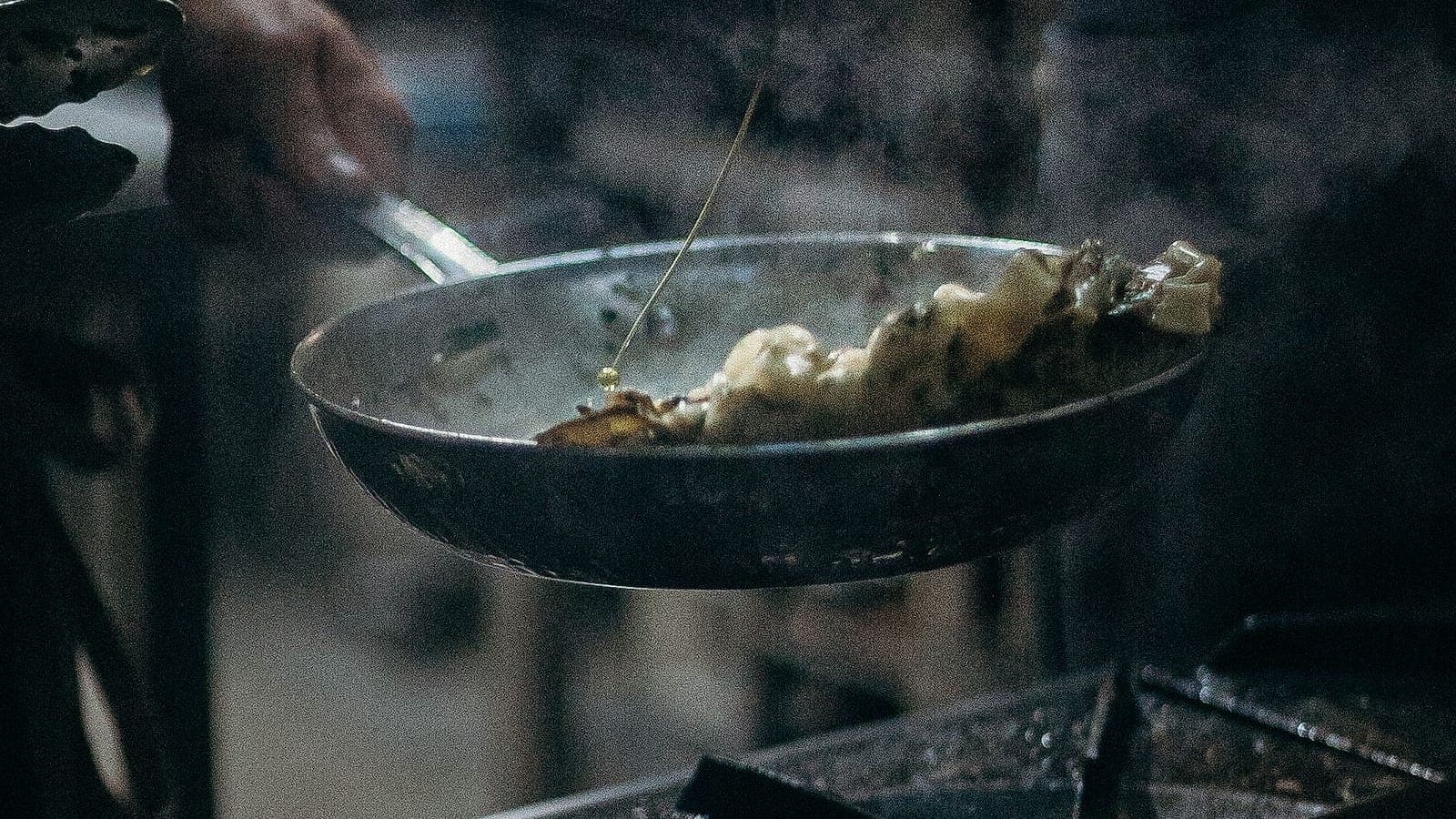 Oil being poured into a well-used frying pan on a stovetop