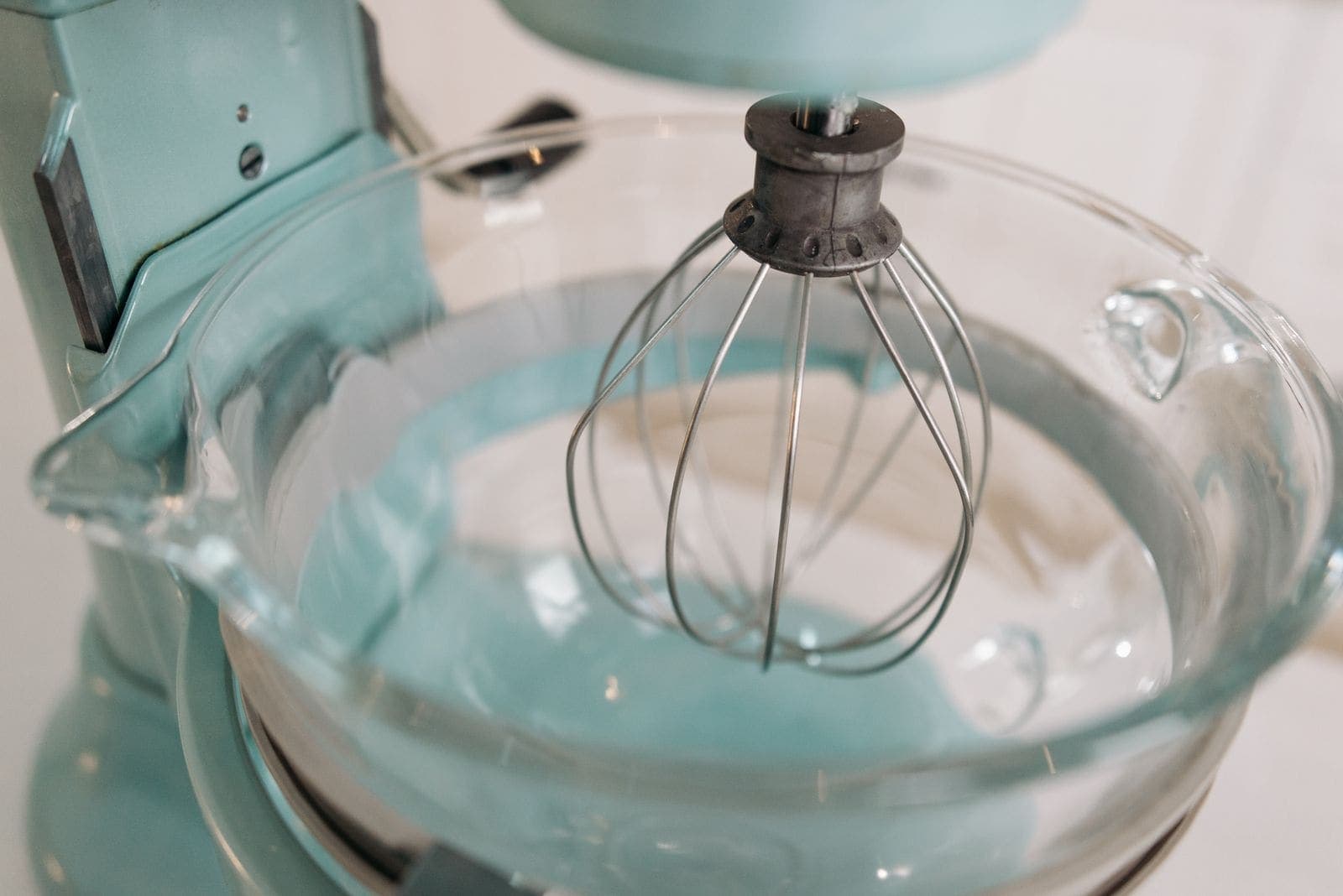 A stand mixer fitted with a glass bowl and wire whip